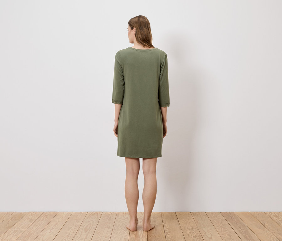 Eine Frau steht mit dem Rücken zur Kamera und trägt ein olivgrünes Kleid mit Dreiviertelärmeln.