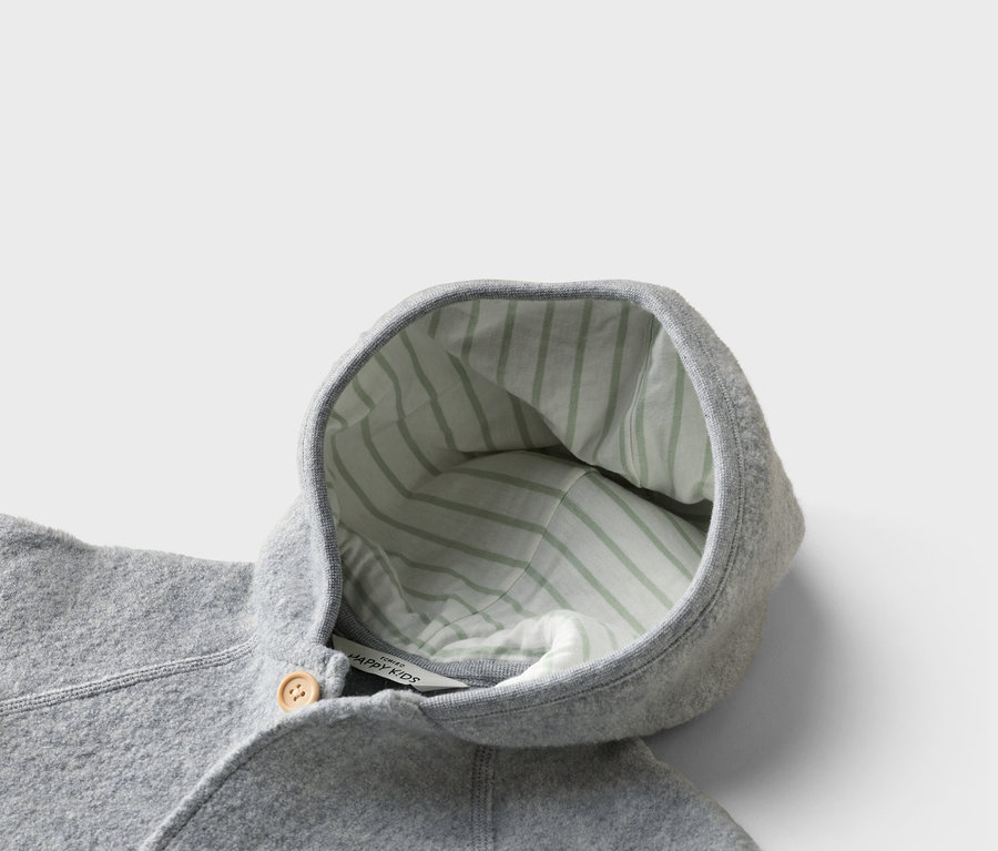 Nahaufnahme einer grauen Kinderjacke mit Kapuze, die mit einem hellgrün gestreiften Stoff gefüttert ist und einen Holzknopf hat.