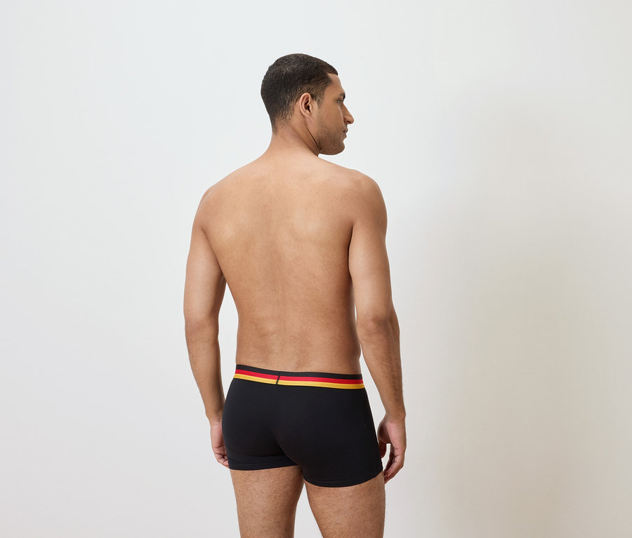 Mann von hinten, mit nacktem Oberkörper, trägt schwarze Boxershorts mit einem schwarz-rot-goldenem Bund.