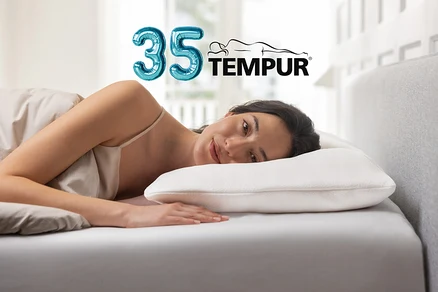 Frau liegt seitlich im Bett, den Kopf auf einem weißen Kissen ruhend und blickt zum Betrachter. Ein blauer „35“-Ballon und das TEMPUR-Logo sind im Hintergrund zu sehen.