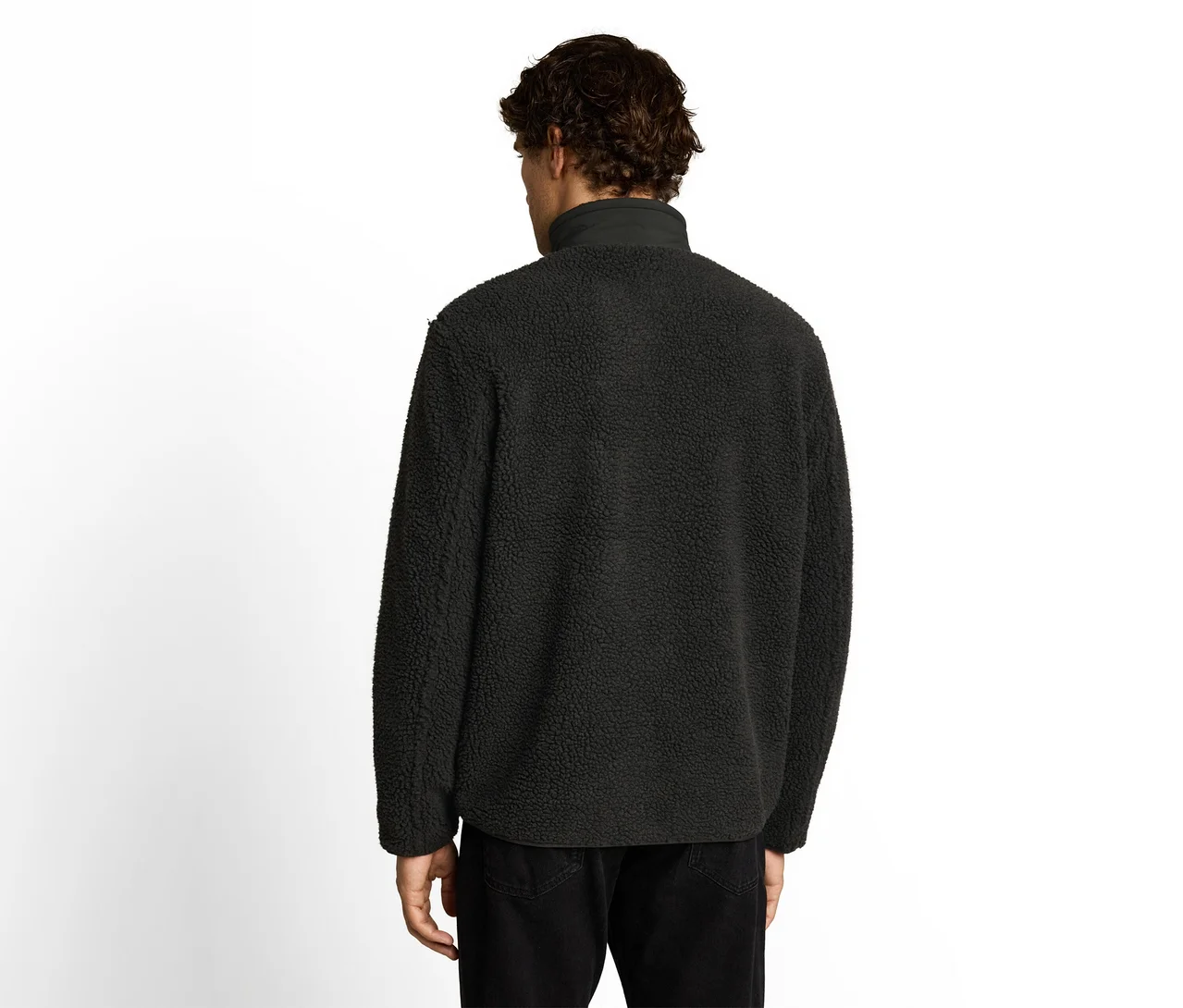 Mann von hinten, trägt eine schwarze Fleecejacke mit Stehkragen und schwarze Hose. Er hat dunkle, lockige Haare.