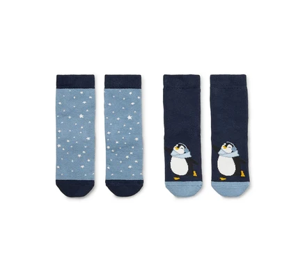 Zwei Paar Socken liegen nebeneinander. Links ein hellblaues Paar mit weißen Sternen, rechts ein dunkelblaues Paar mit Pinguinmotiv. Beide Paare haben dunkelblaue Bündchen und Zehen.