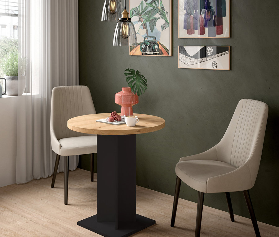 Ein kleiner Essbereich mit einem runden Holztisch, zwei beigefarbenen Polsterstühlen und einer dunkelgrünen Wand. Auf dem Tisch stehen eine rosa Vase, eine weiße Tasse und Macarons. Drei gerahmte Bilder und zwei Glas-Pendelleuchten hängen an der Wand, links ist ein Fenster.