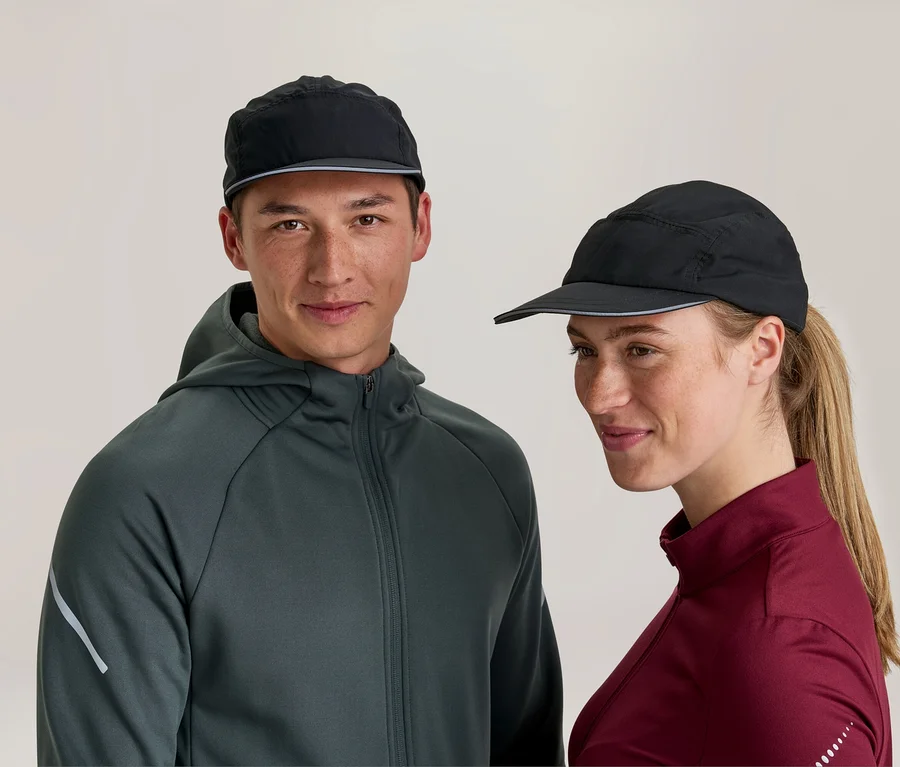 Ein Mann und eine Frau tragen schwarze Sportkappen. Der Mann trägt eine dunkelgraue Kapuzenjacke und blickt nach vorne, während die Frau ein bordeauxrotes Langarmshirt trägt und leicht lächelnd zur Seite blickt.