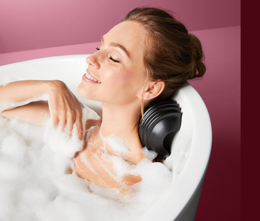 Frau lächelt und liegt in einer mit Schaum gefüllten Badewanne mit Badewannen-Massagekissen.