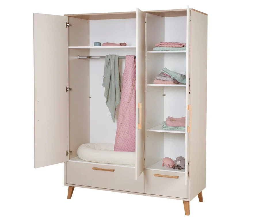 Ein offener, hellbeiger Kleiderschrank mit Holzdetails, ausgestattet mit einer Kleiderstange mit grüner Decke und rosa Schlafsack, einem weißen Babynest, Regalböden mit gefalteten rosa und grünen Textilien sowie zwei Spielzeugen (ein rosa Schwein und ein grauer Bär).