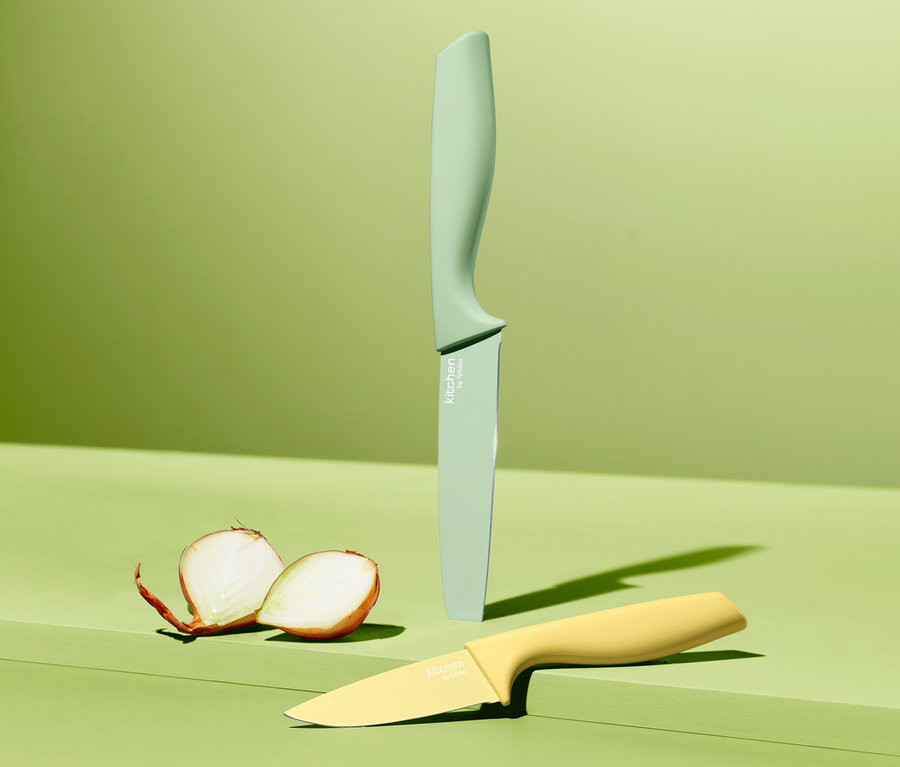Zwei Küchenmesser aus dem Küchenmesser-Set und eine halbierte Zwiebel auf grünem Hintergrund.
