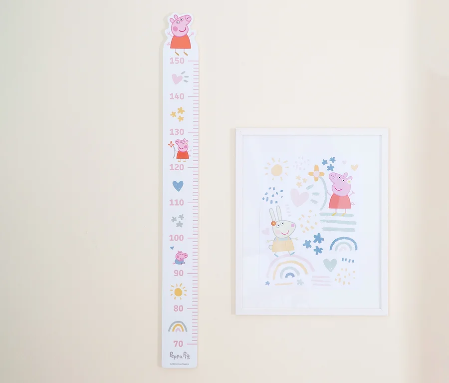 An einer hellbeigen Wand hängen ein Peppa Pig-Wachstumsdiagramm und ein gerahmtes Bild.