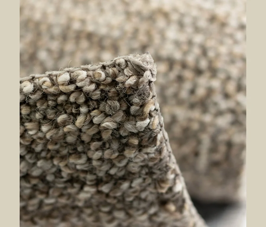 Nahaufnahme eines Teppichs mit Schlingenflor in gesprenkelten Braun- und Beigetönen, ein gefalteter Bereich zeigt die Textur.