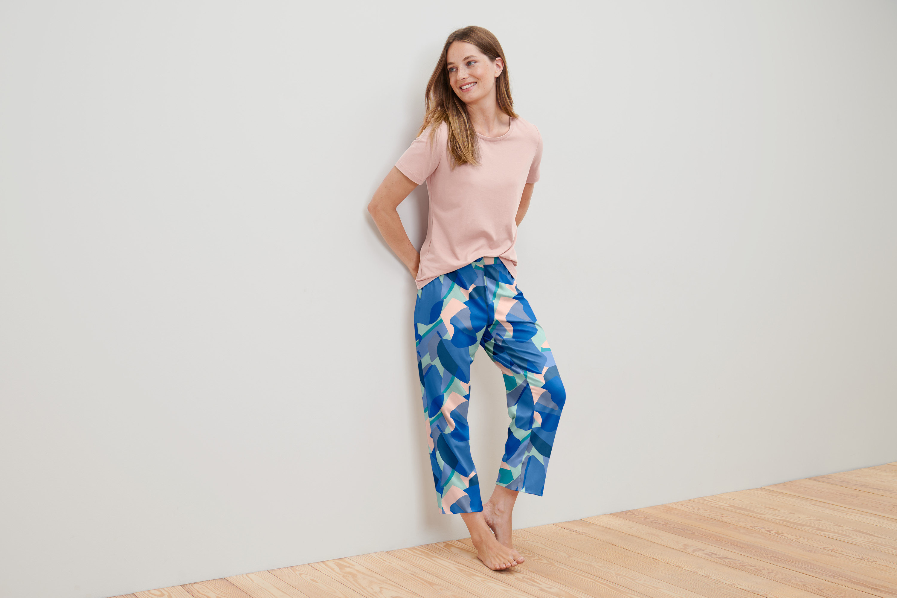 Frau lehnt in einem Pyjama an einer Wand.