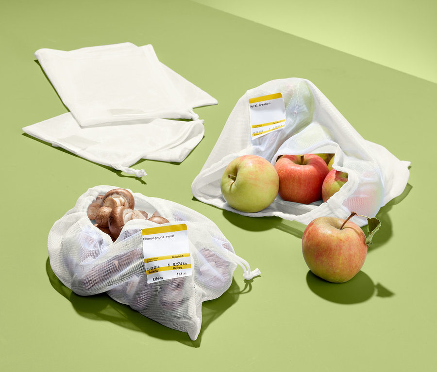 Auf grünem Grund liegen zwei lose, weiße Netze und zwei befüllte. Ein Netz enthält Äpfel, das andere braune Champignons. Es handelt sich um 4 Obst- und Gemüsenetze.