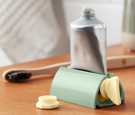 Silberne Tube in einem grünen Tubenpresser auf einem Holzregal.