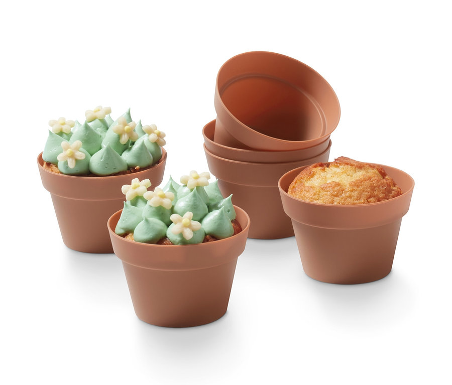 Zwei wie Kakteen dekorierte Muffins nebeneinander, dahinter ein Stapel aus vier Blumentopf-Muffinformen und ein gebackener Muffin.