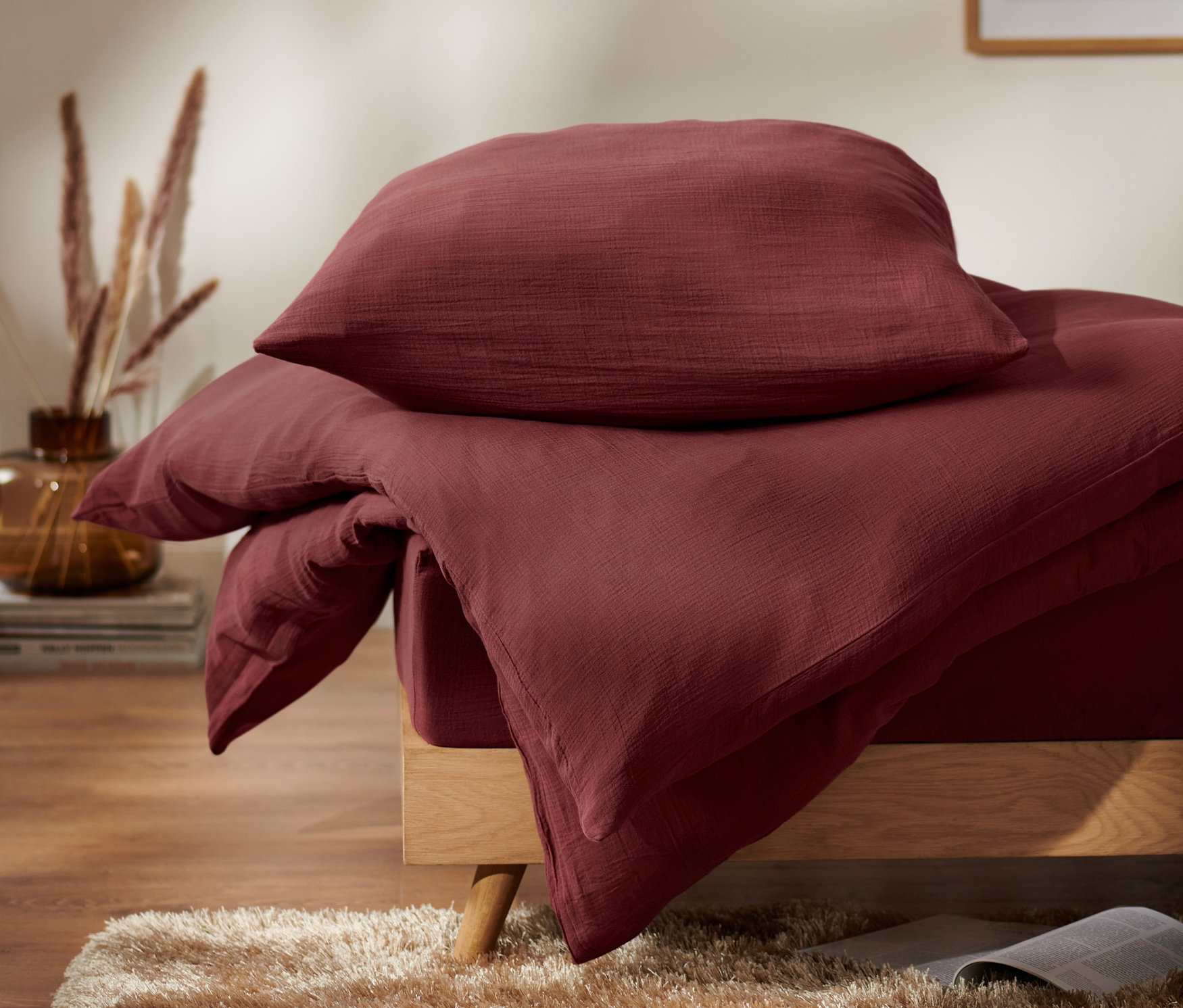 Detailaufnahme von bordeauxroter Musselin-Bettwäsche mit Kissen.