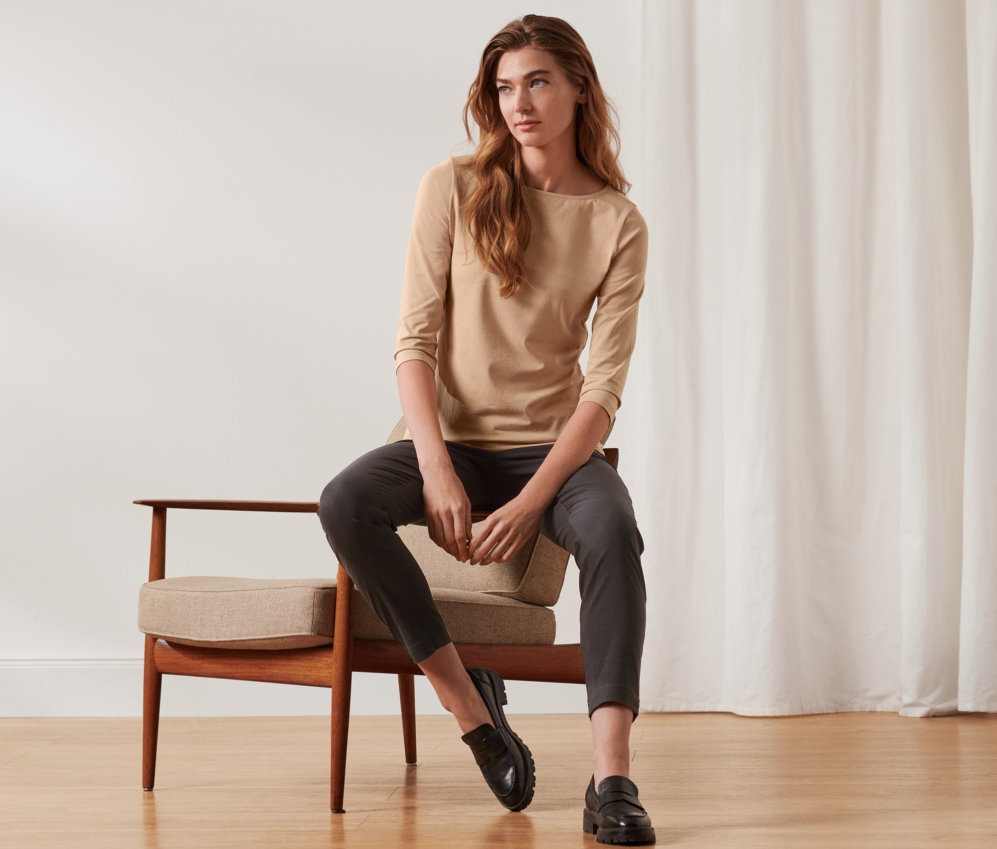 Frau sitzt auf einem Stuhl und trägt ein beiges Shirt mit 3/4-Arm.