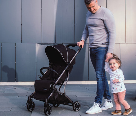 Mann schiebt schwarzen Kinderwagen »Boogy« und hält die Hand eines kleinen Kindes.