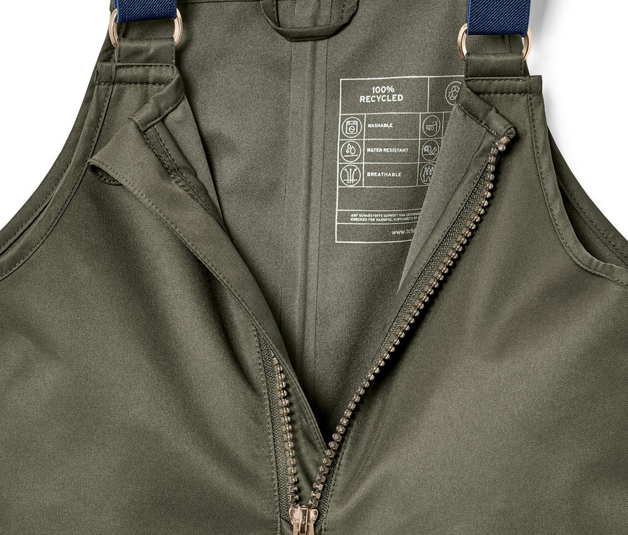 Nahaufnahme einer olivgrünen Regenhose mit geöffnetem Reißverschluss und blauen Trägern.