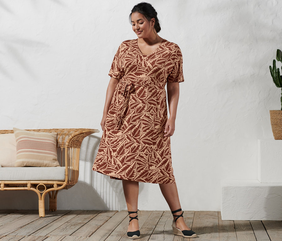 Frau steht und trägt ein bedrucktes Jerseykleid und Espadrilles mit Keilabsatz.