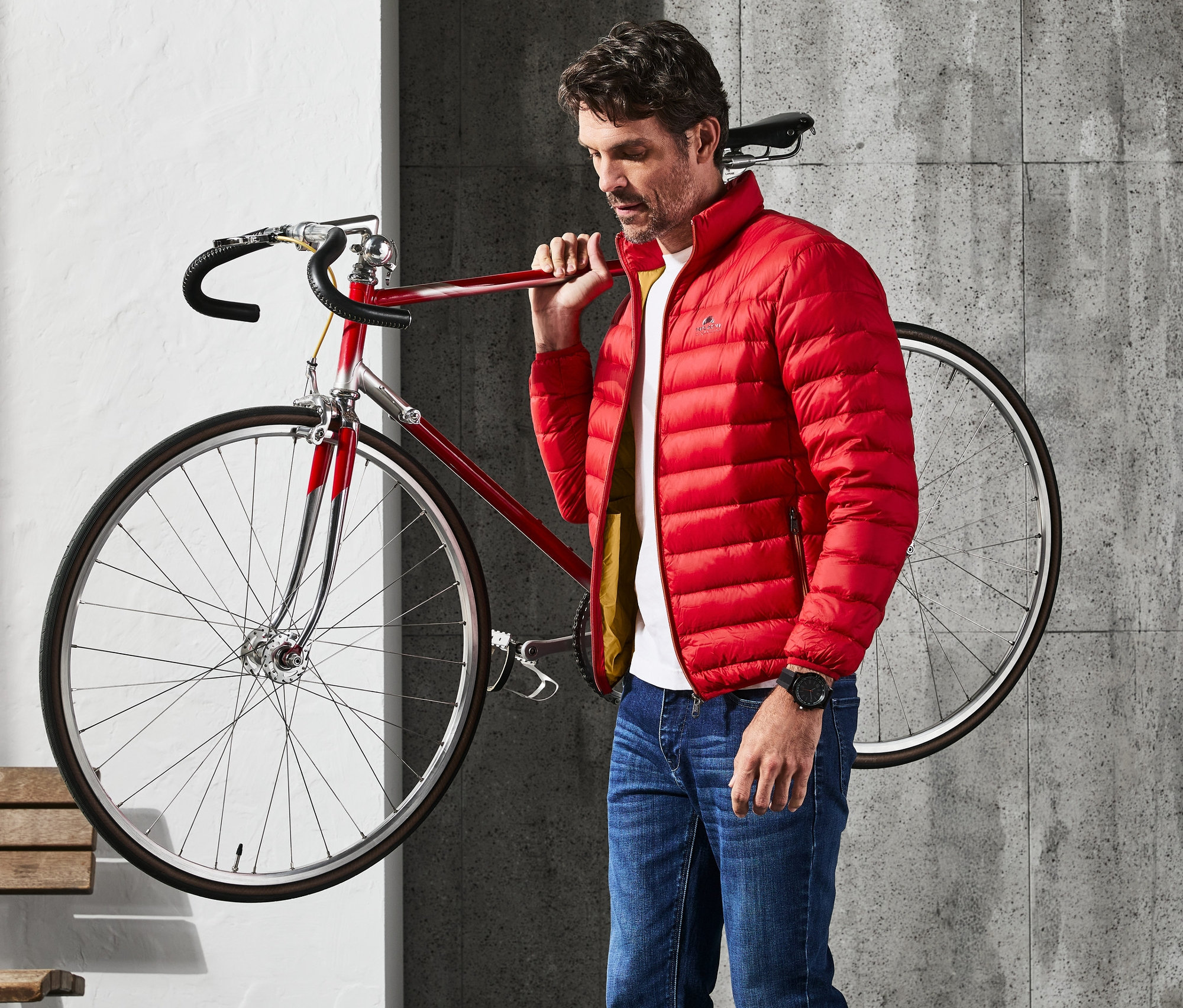 Mann mit roter Daunenjacke trägt ein rotes Fahrrad über der Schulter.