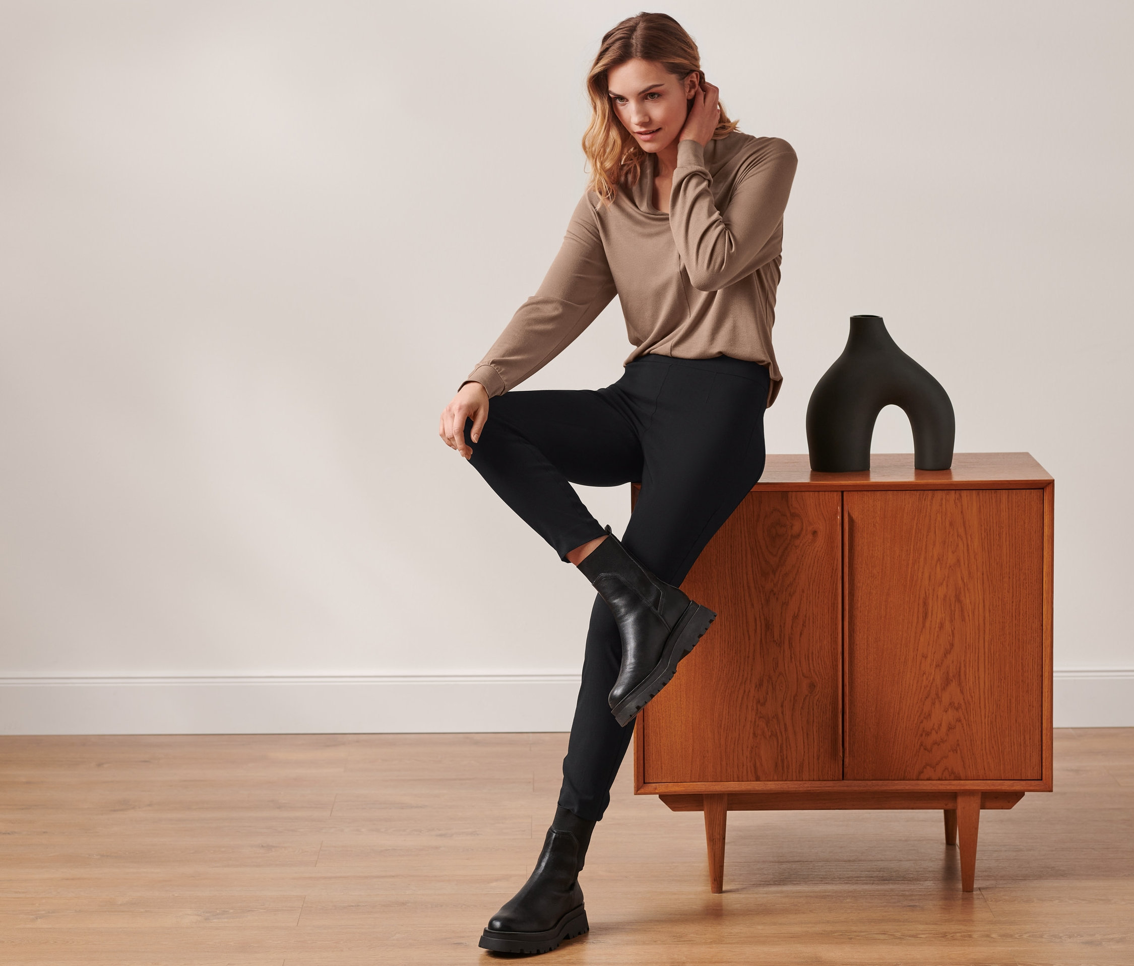 Frau sitzt auf einem Schrank, trägt eine Stretchhose, schwarz.