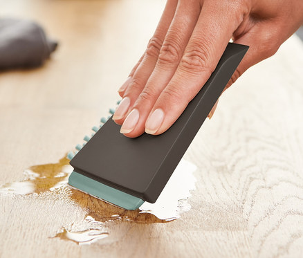 Eine Frau wischt mit einer Universal-Küchenbürste eine Flüssigkeit von einer Holzoberfläche.