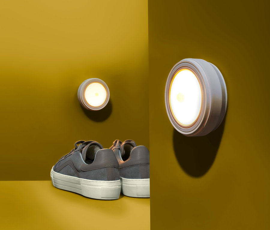 Zwei LED-Multifunktionsleuchten sind an einer gelben Wand montiert, darunter stehen Schuhe.