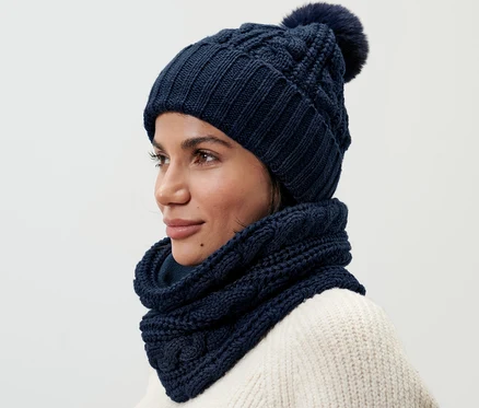 Frau trägt einen Strickschlauchschal und eine passende Strickmütze mit Bommel.