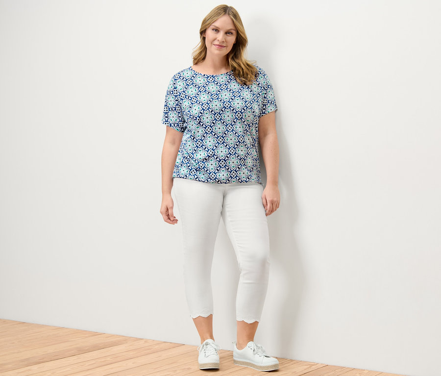 Frau posiert in einem Blusenshirt mit Alloverprint und einer 7/8-Treggings mit Lochstickerei.