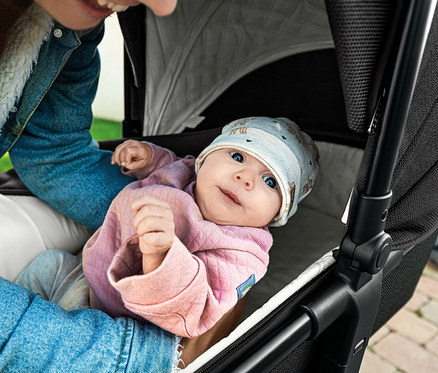Lächelndes Baby liegt im Osann Kombi-Kinderwagen »Vamos«.