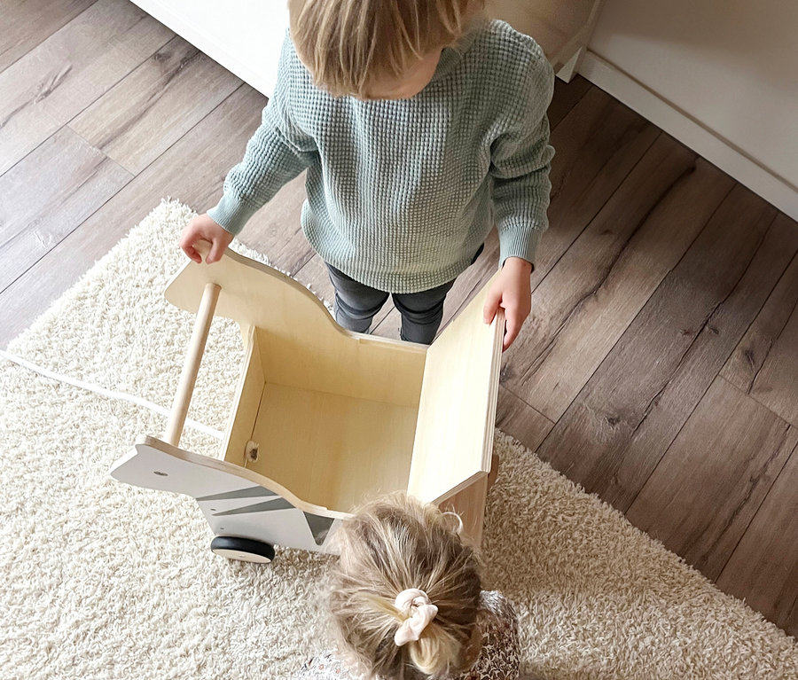 Junge schiebt small foot Spielzeugkiste Zebra »Wildlife«, während Mädchen auf dem Teppich sitzt.