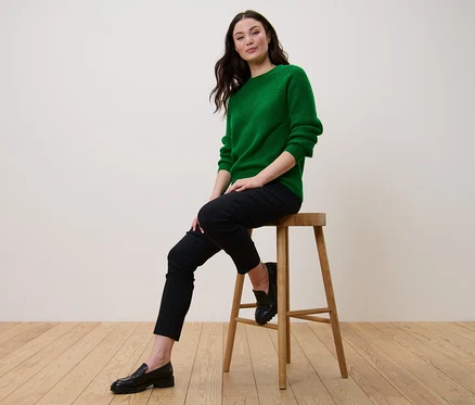 Eine Frau sitzt auf einem Hocker und trägt einen grünen Strickpullover.