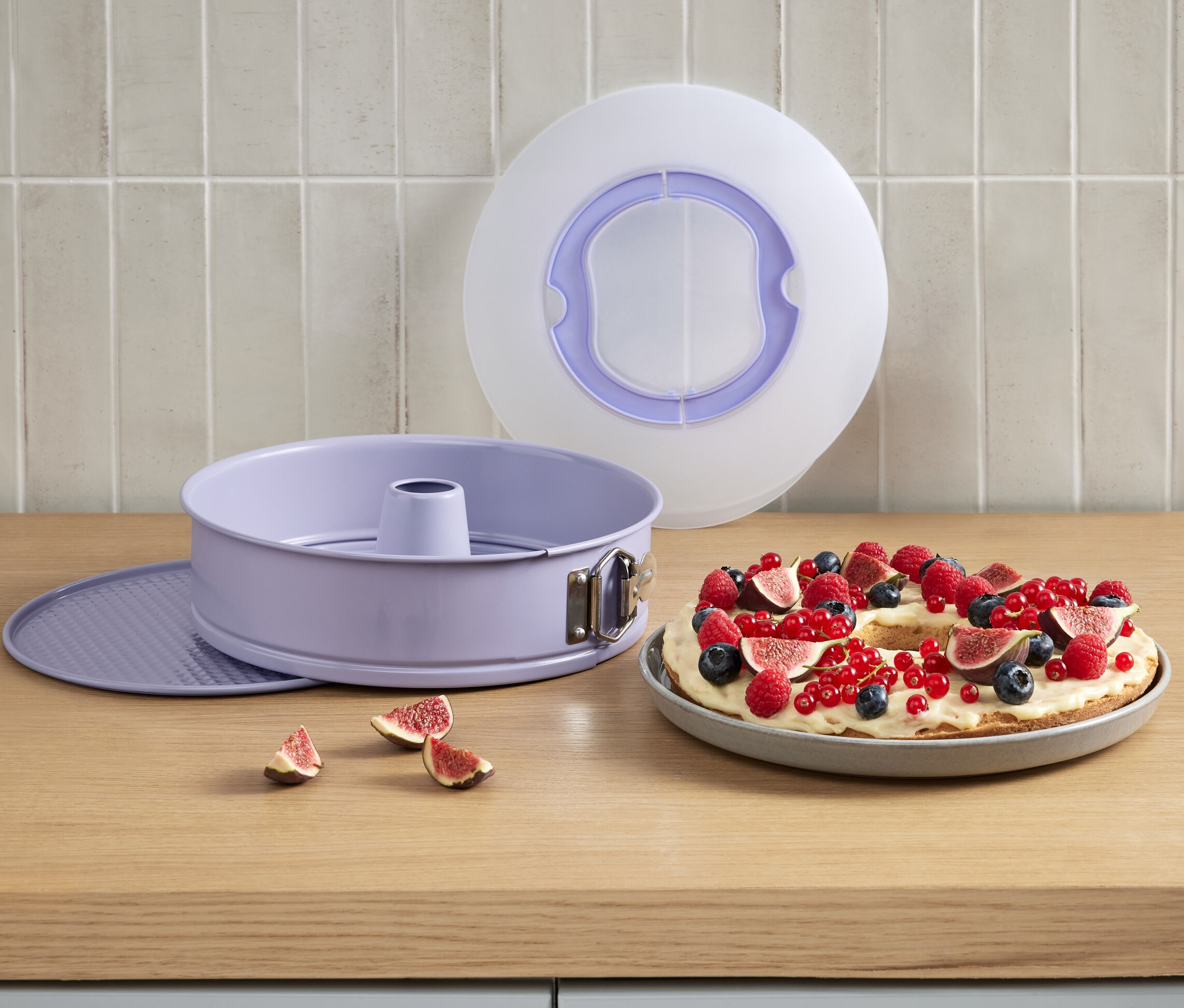 Eine Springform mit Transportdeckel neben einem Kuchen mit Früchten.