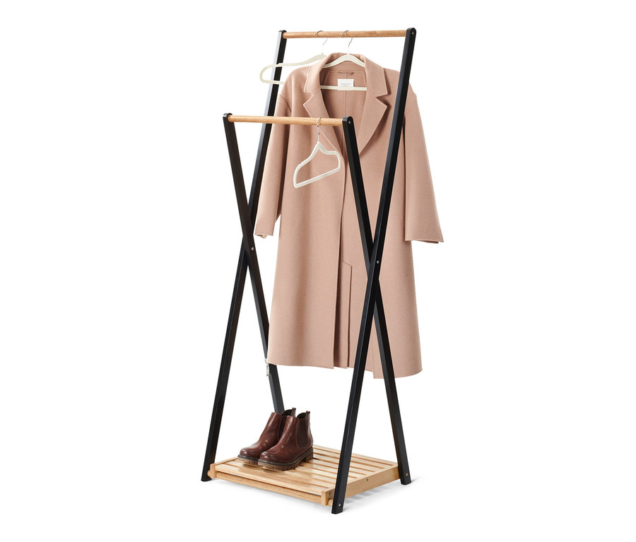 Ein Mantel hängt an einem Bügel auf einem Kleiderständer, darunter Schuhe.