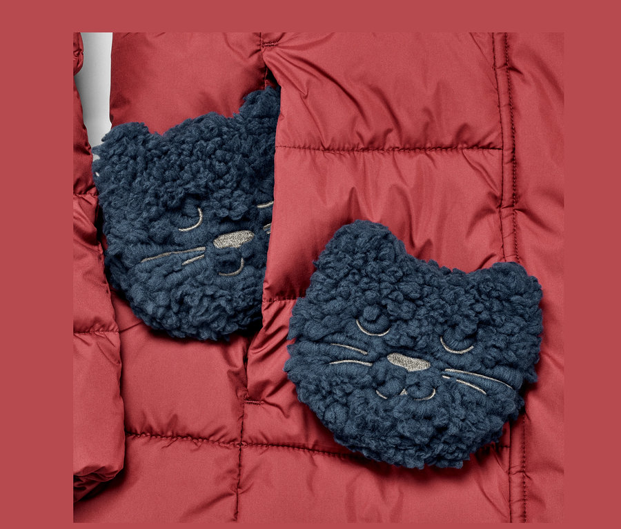 Zwei Taschenheizkissen, »Katze« liegen auf einer roten Jacke.