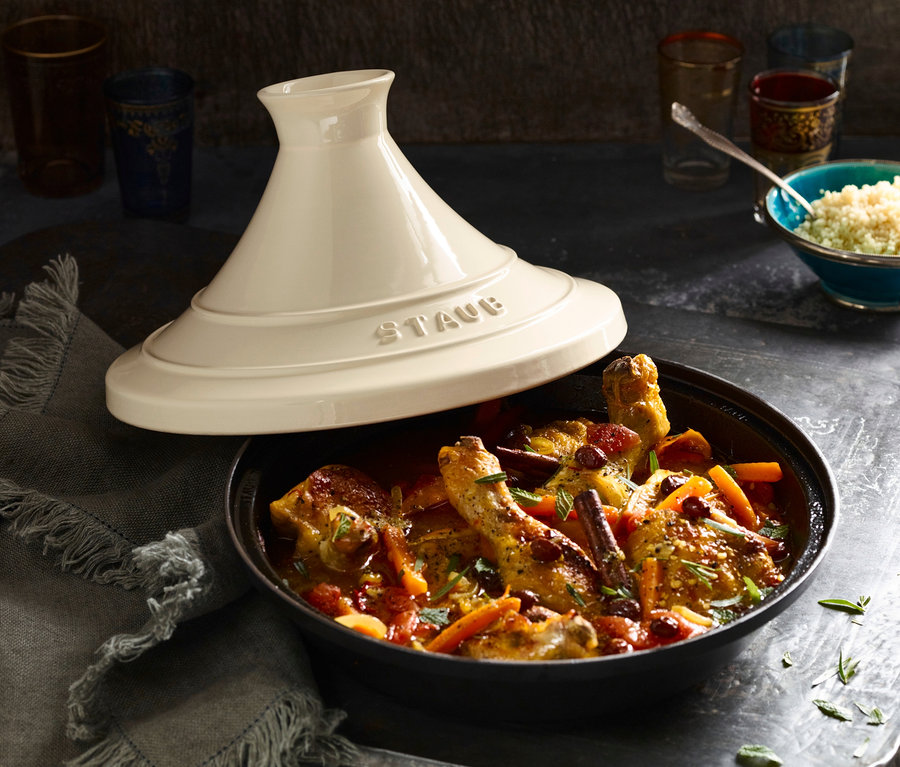 Tajine mit Hähnchen, Gemüse und Gewürzen, STAUB Deckel daneben. Im Hintergrund eine Schüssel mit Couscous und Gläser.
