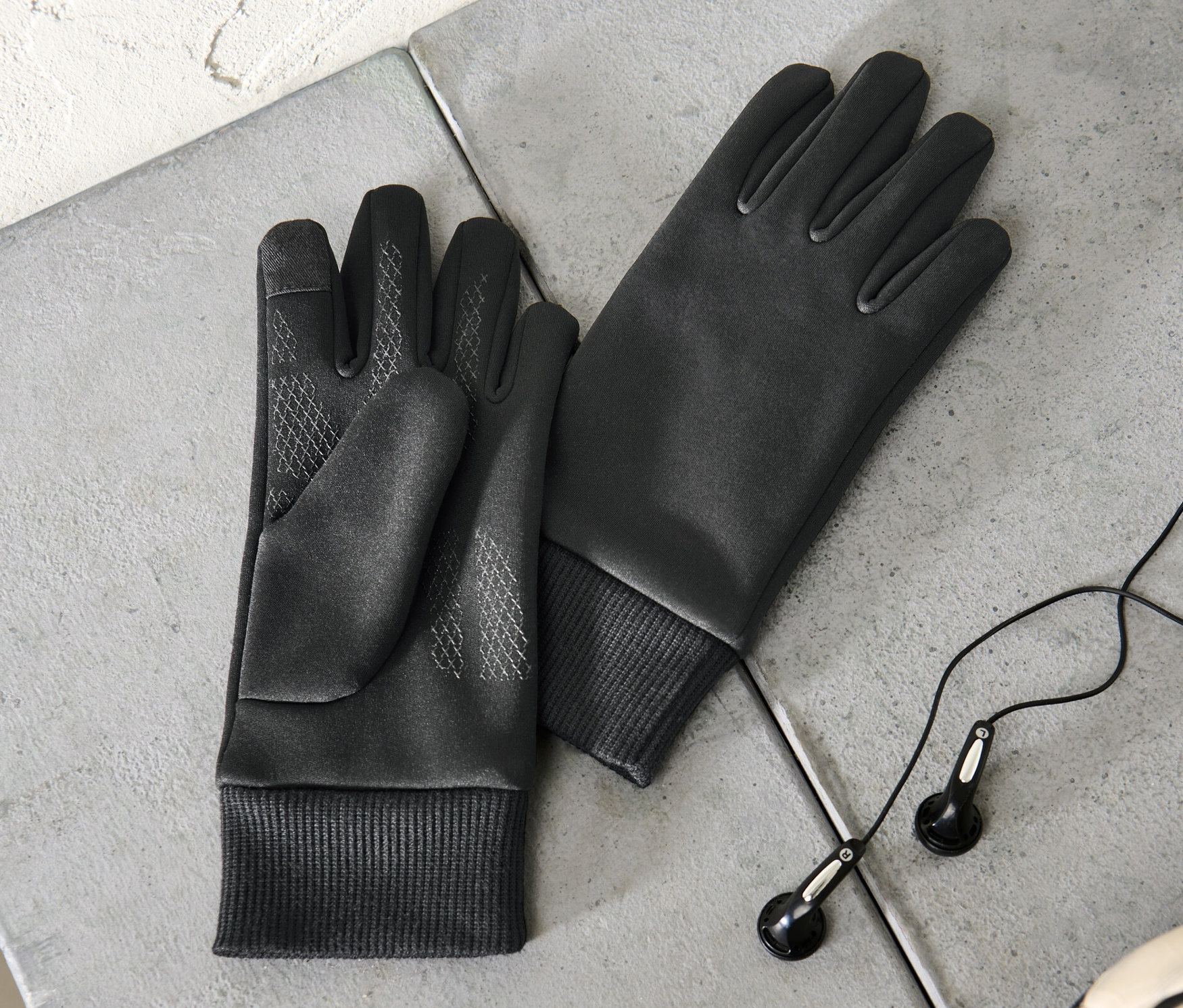 Zwei Kinder-Windprotection-Thermohandschuhe liegen auf einer grauen Oberfläche neben Kopfhörern und einem Teil eines Fußballs.