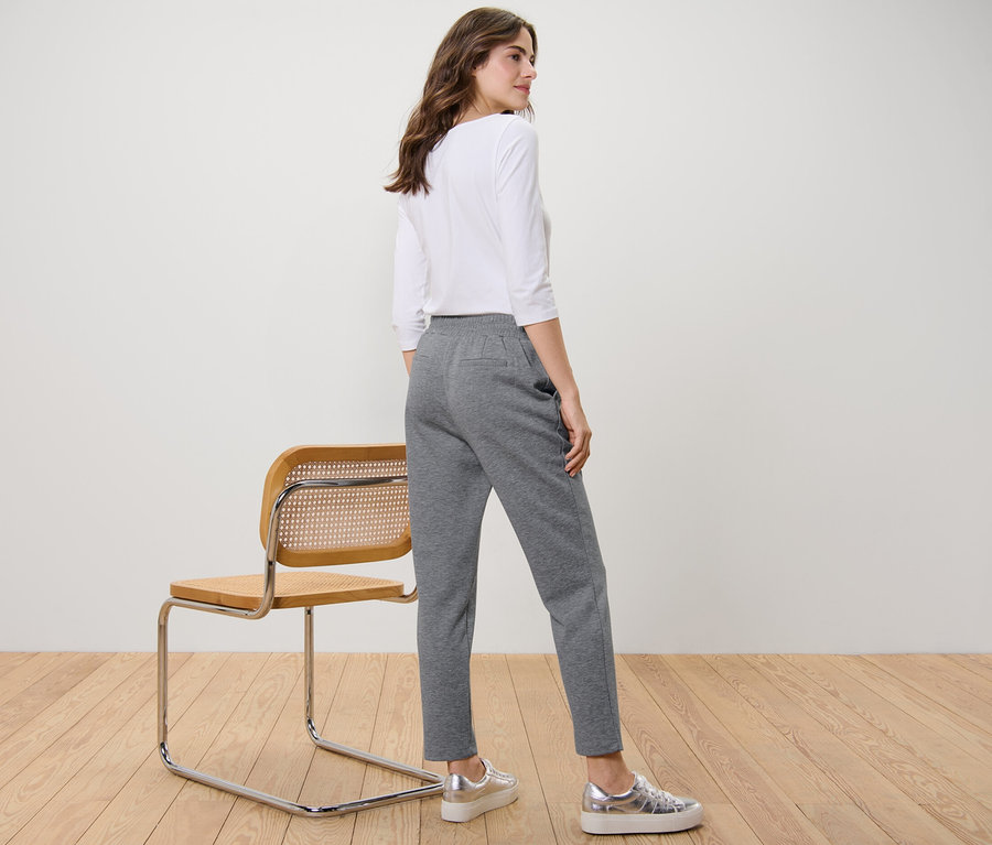 Frau steht seitlich und trägt eine graue Joggpants.