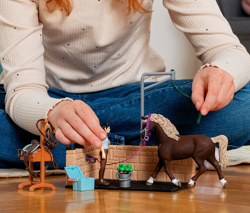 Eine Person spielt mit einem Schleich »Horse Club« Waschplatz mit braunem Pferd.