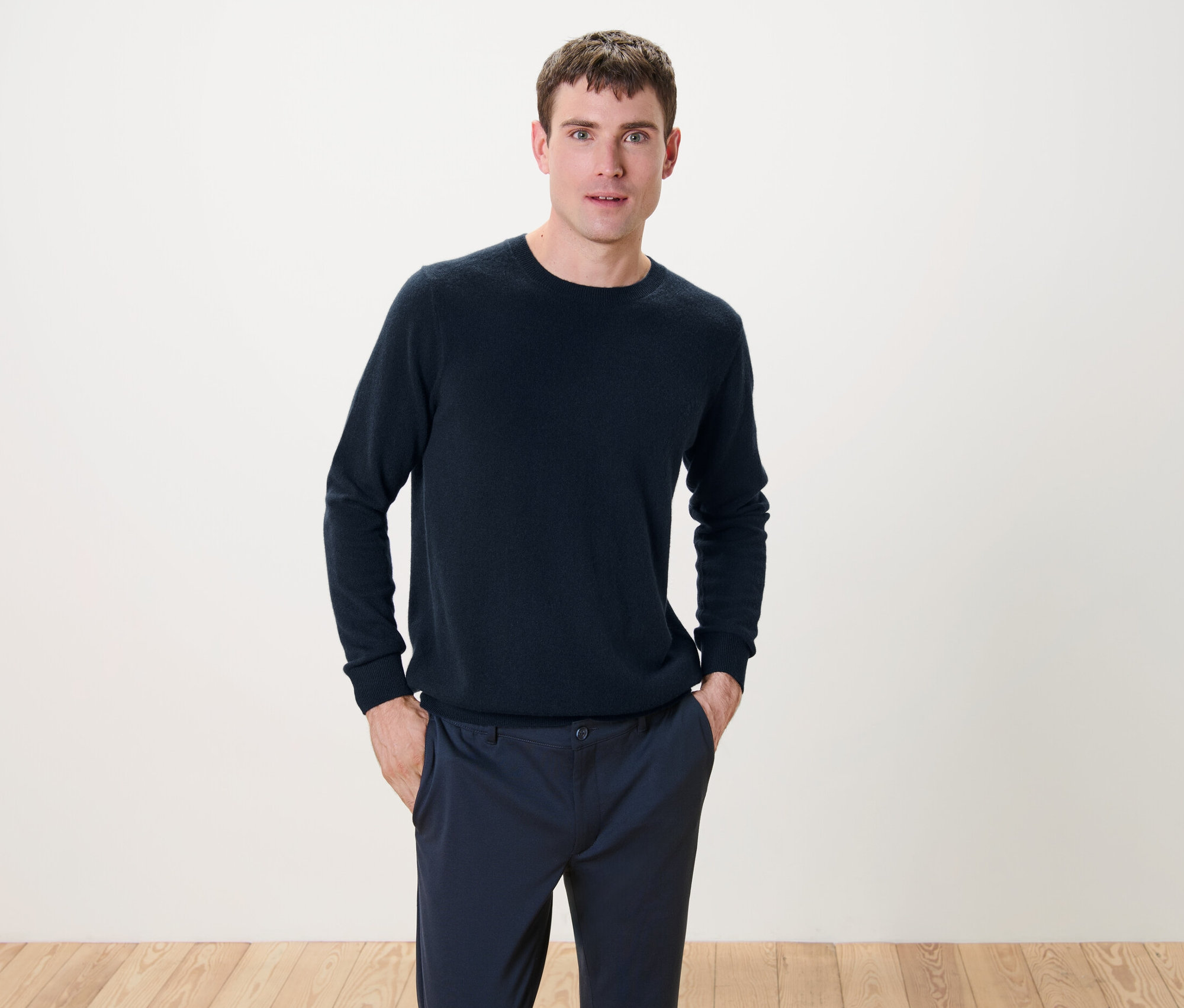 Ein Mann steht mit den Händen in den Hosentaschen und trägt einen marineblauen Cashmere-Pullover mit Rundhalsausschnitt.