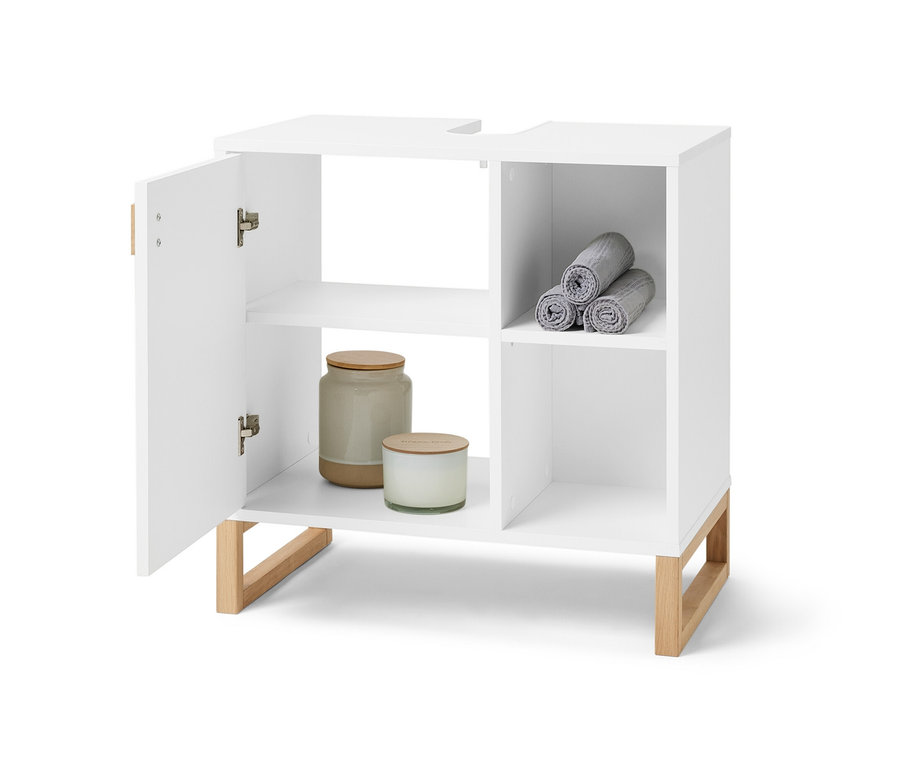 Offener, weißer Waschbeckenunterschrank mit Tür und Seitenfach. Im Seitenfach befinden sich zusammengerollte graue Handtücher, im Schrankinneren Kerzen und eine Dose.