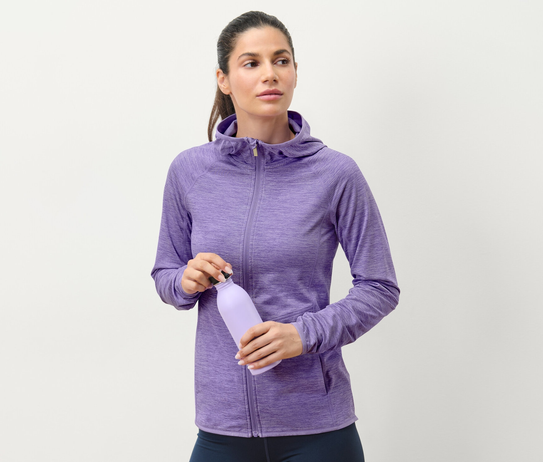 Frau hält eine lila Wasserflasche und trägt eine flieder melierte Sportjacke.