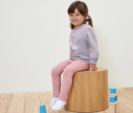Mädchen sitzt auf einem Holzhocker und trägt Kinder-Jeggings ‒ Fit »Ida« mit Punkten.