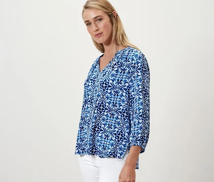 Blonde Frau posiert in blau bedruckter Tunika-Bluse.