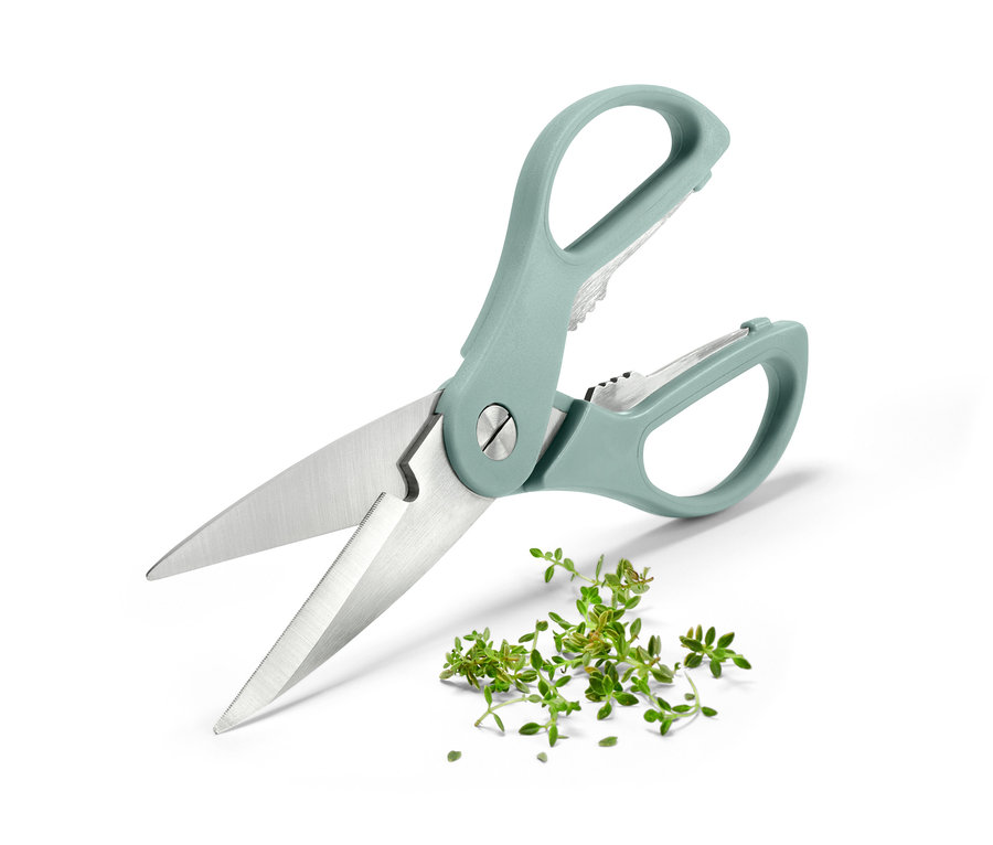 Nahaufnahme einer Küchen- und Kräuterschere mit blaugrünem Griff, die auf einer weißen Oberfläche neben gehackten Kräutern liegt.