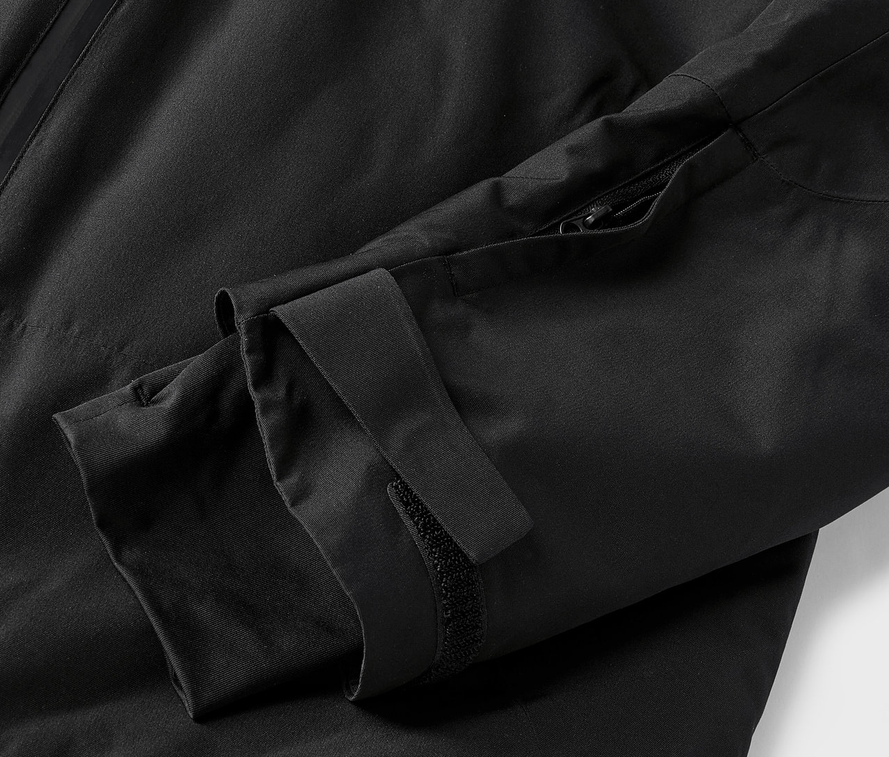 Detailaufnahme einer schwarzen Jacke mit Ärmel und Reißverschluss.