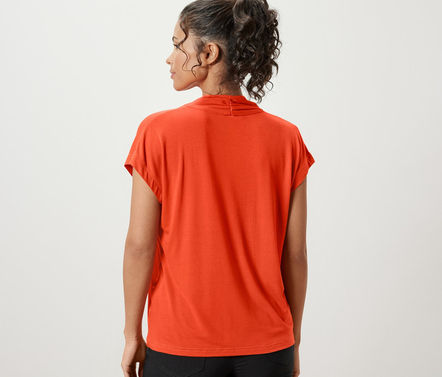 Rückansicht einer Frau, die ein oranges Blusenshirt mit V-Ausschnitt und schwarze Shorts trägt.