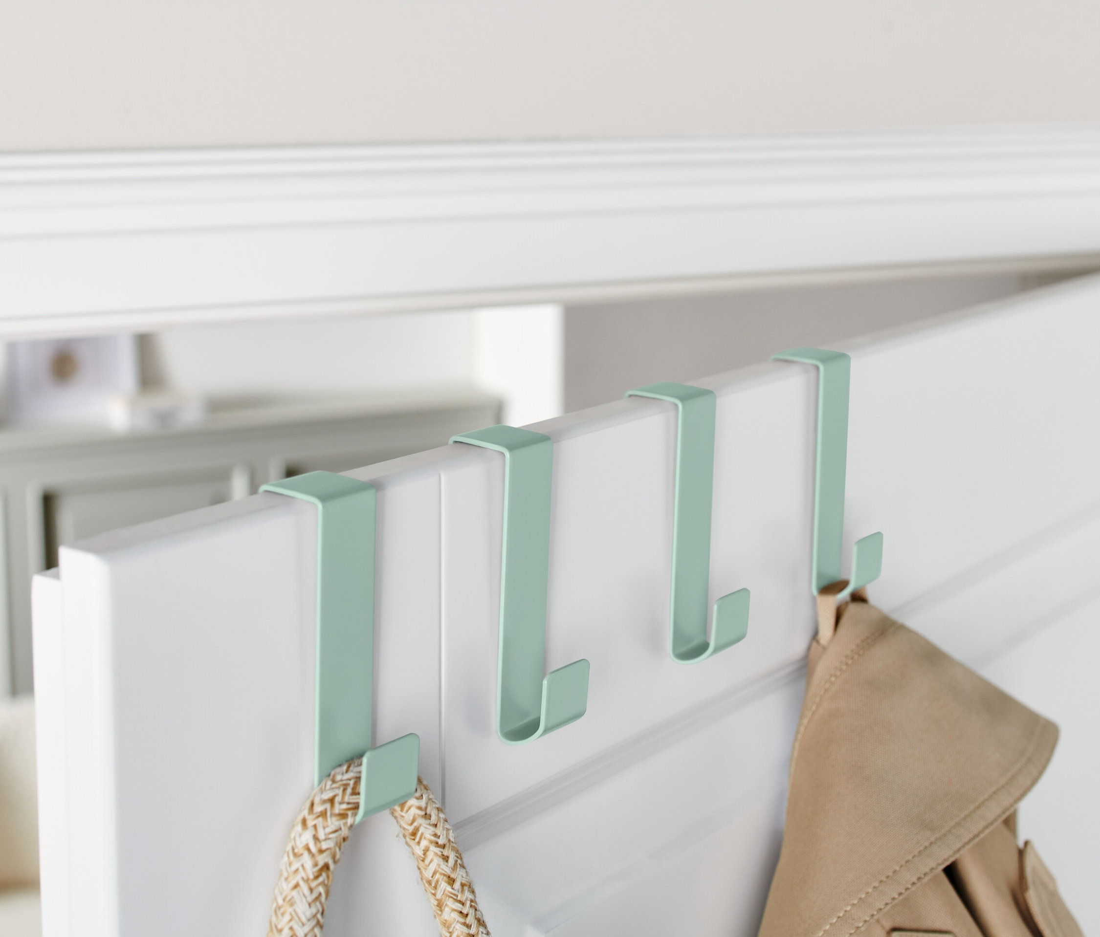 Vier grüne Türhaken hängen an der Oberkante einer weißen Tür.