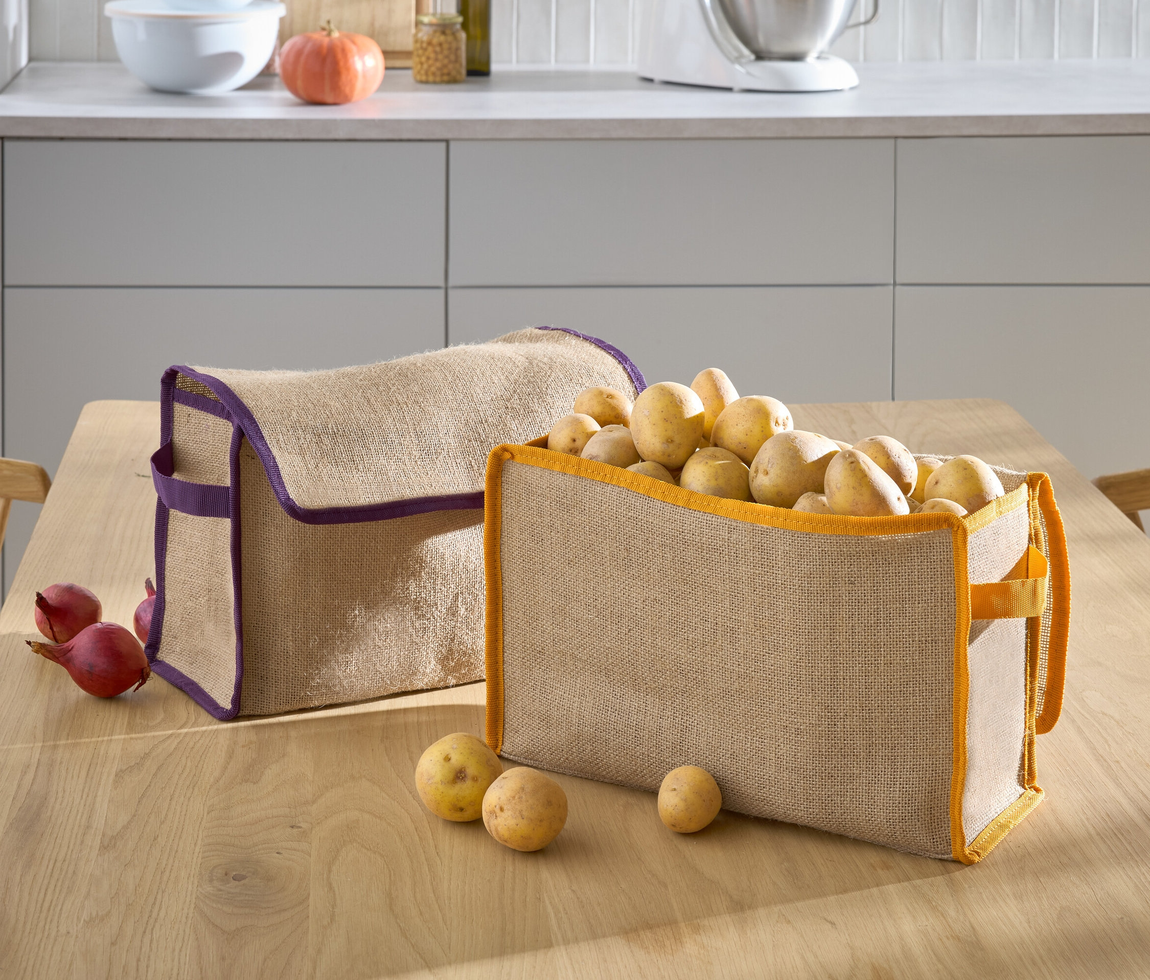 Zwei beige Körbe stehen auf einem Tisch, einer mit lila Rand ist leer und der andere mit orangefarbenem Rand ist mit Kartoffeln gefüllt.