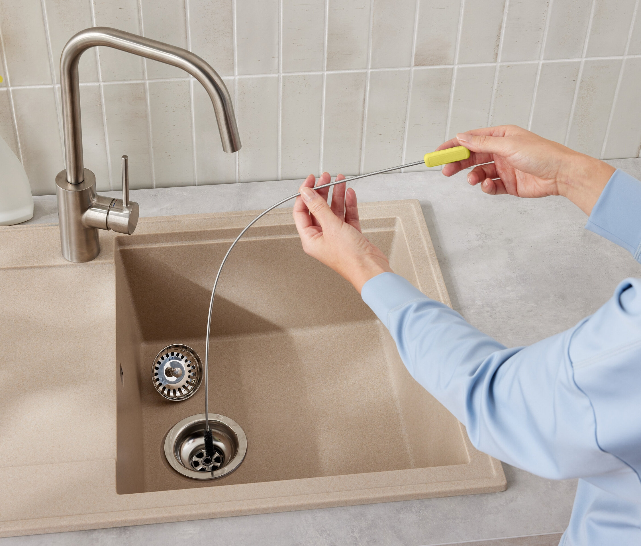 Frau reinigt einen Spülenabfluss mit einem Abflussreinigungswerkzeug mit gelbem Griff.