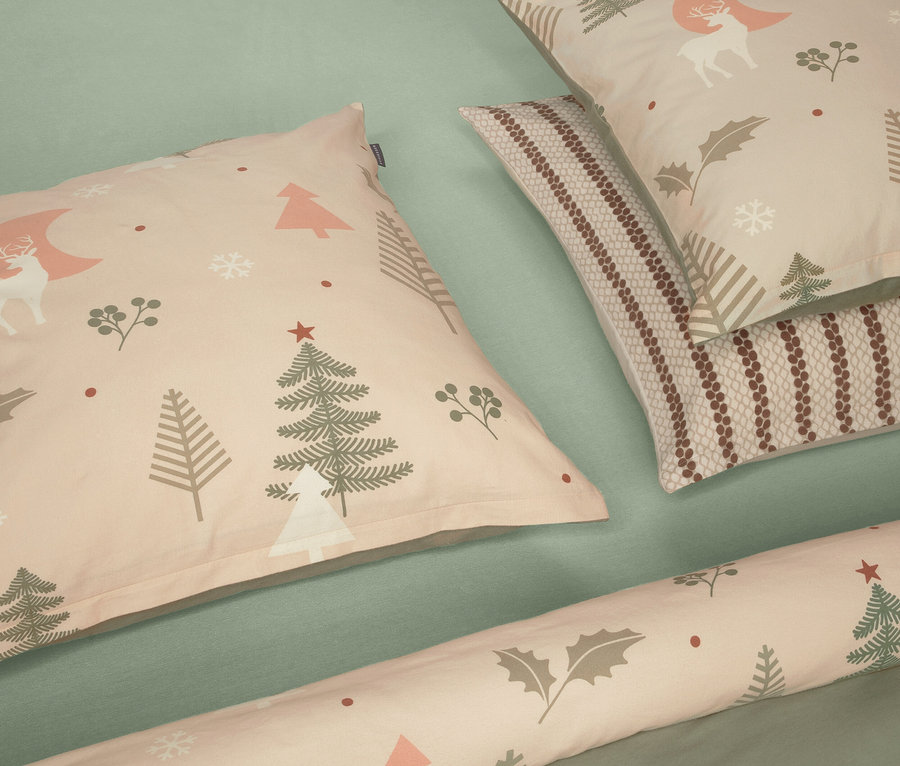 Zwei beige Kissen mit Weihnachtsmotiven und ein schmales Kissen auf grünem Hintergrund.